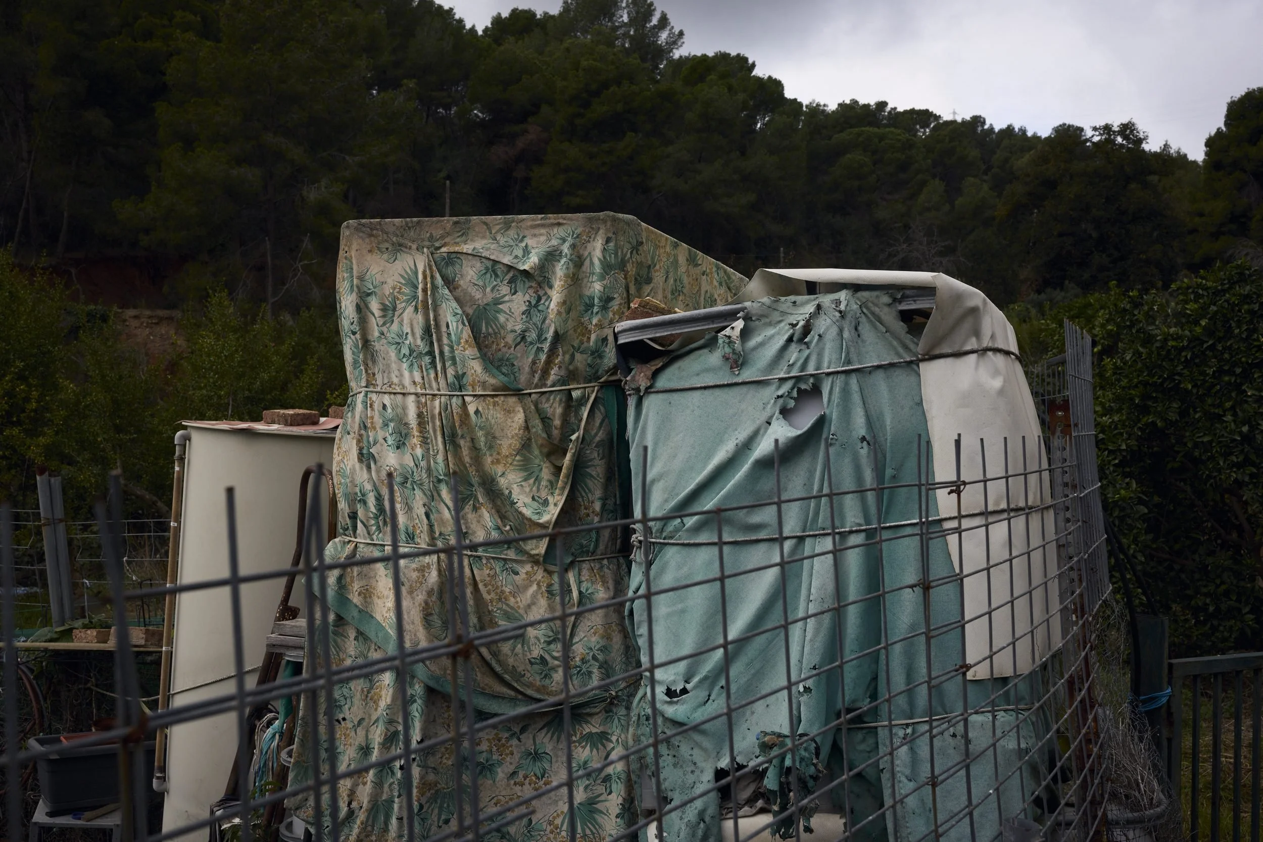 Tarped containers and tanks enclosed by metal fencing with forested hillside in background.