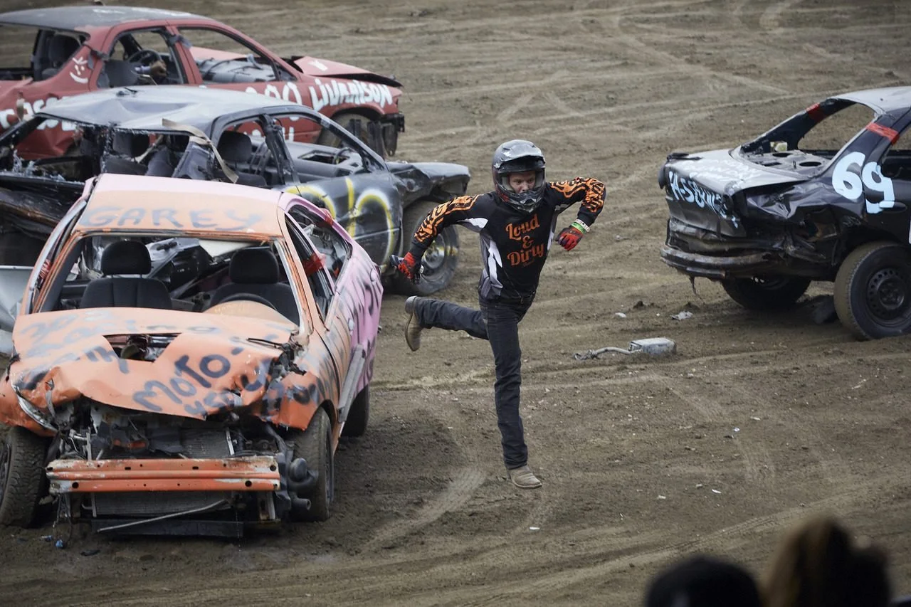 A performer in a helmet jumps between wrecked cars during a demolition derby event.
