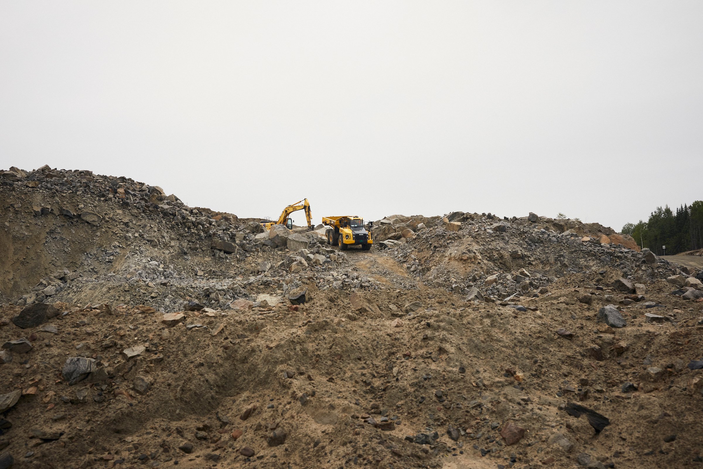 Excavator and hauler work a waste-rock ridge at the Nouveau Monde Graphite mine, Saint-Michel-des-Saints, Quebec.
