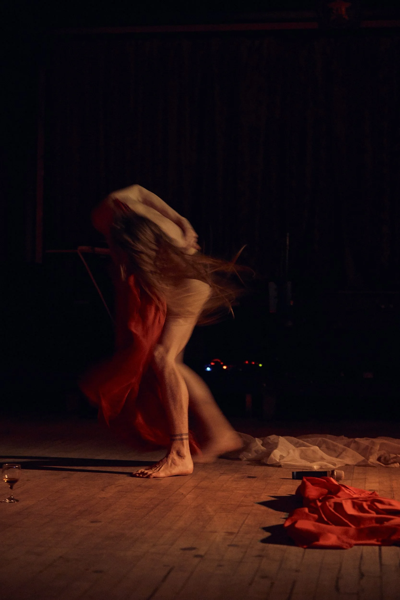 A performer in a red fabric moves dramatically on a dark stage during a dance performance.