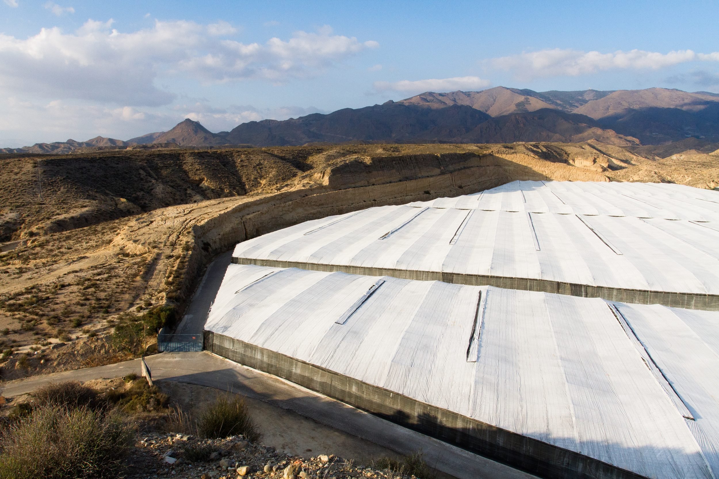 Large white covered reservoir or water storage structure built into arid, mountainous terrain.