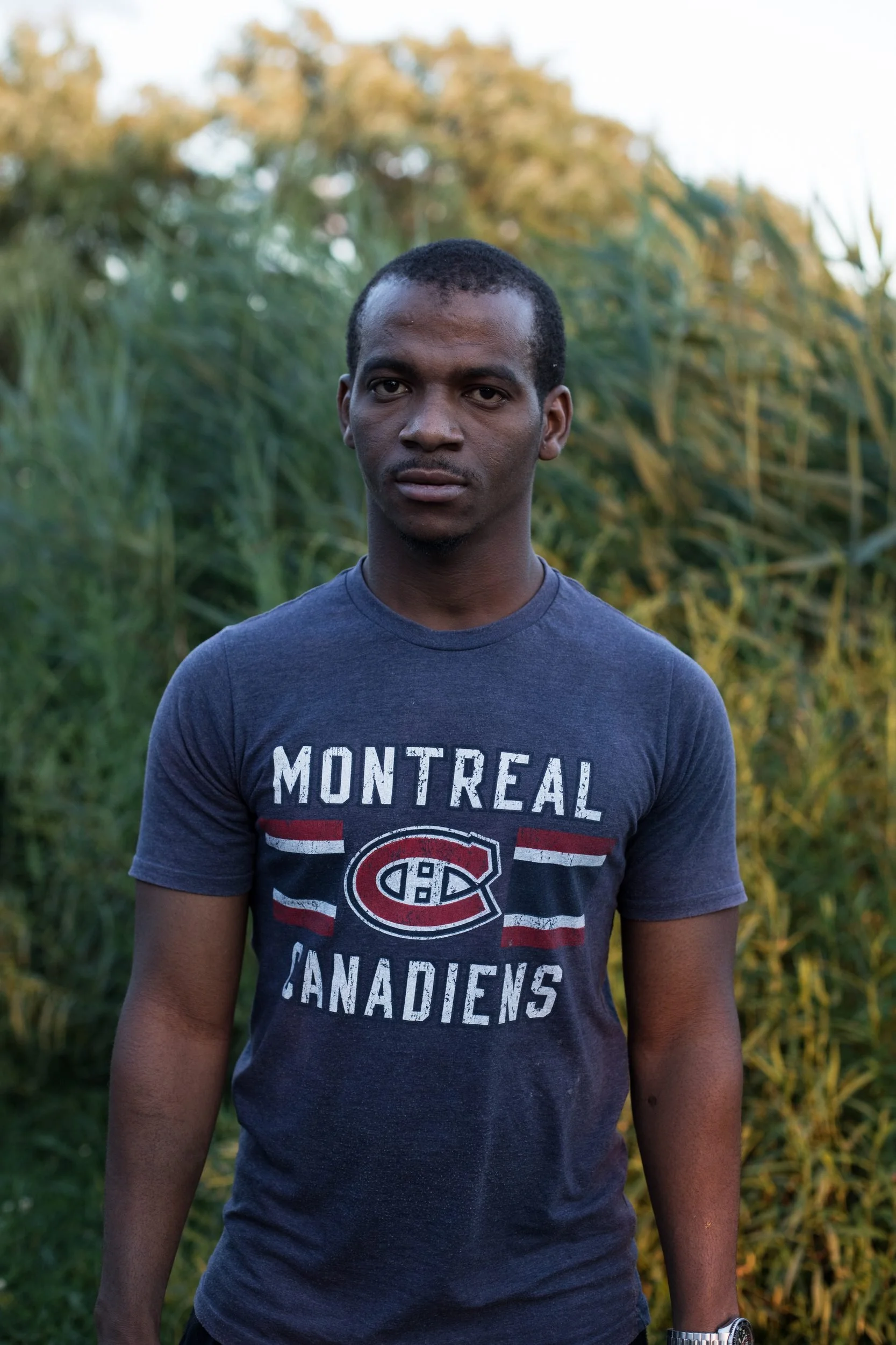 Man in Montreal Canadiens t-shirt stands in front of evergreen trees.