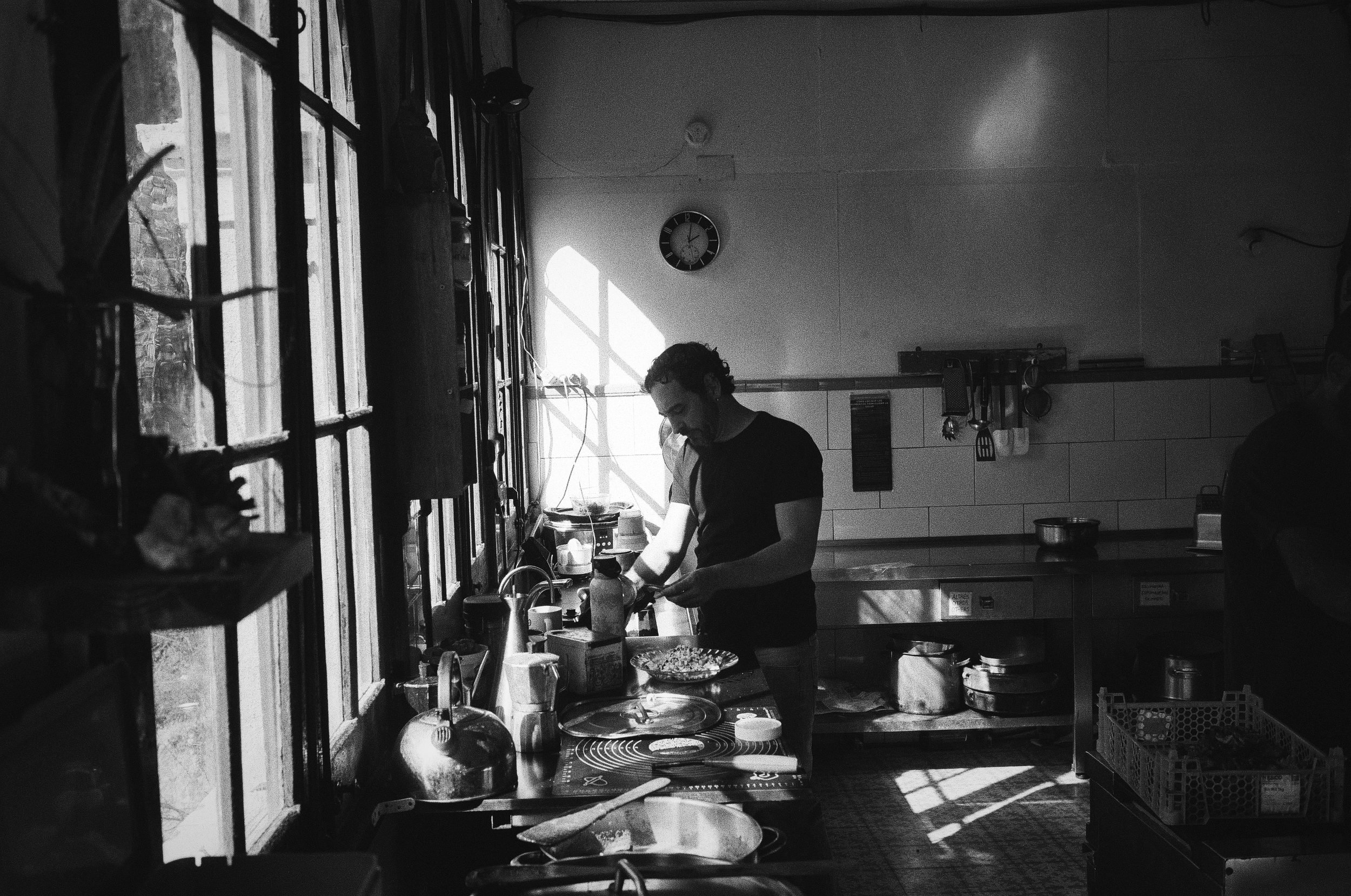 A person in a black shirt works at a kitchen sink by a window in black and white.