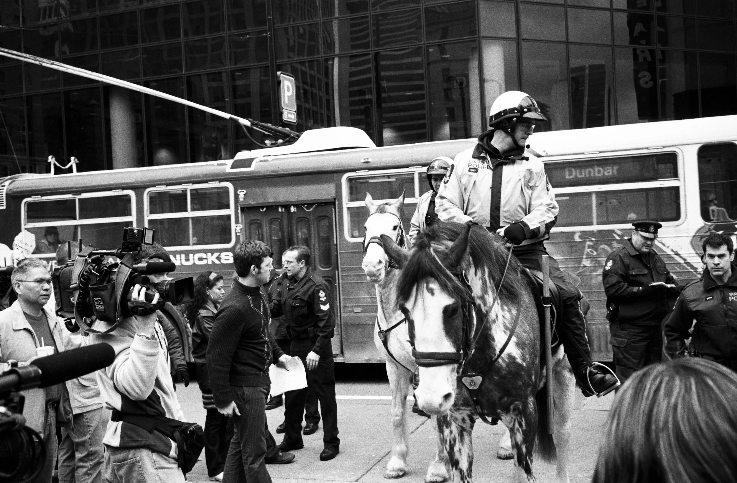 Mounted police officer on horseback among media and officials near a transit bus during a public event.