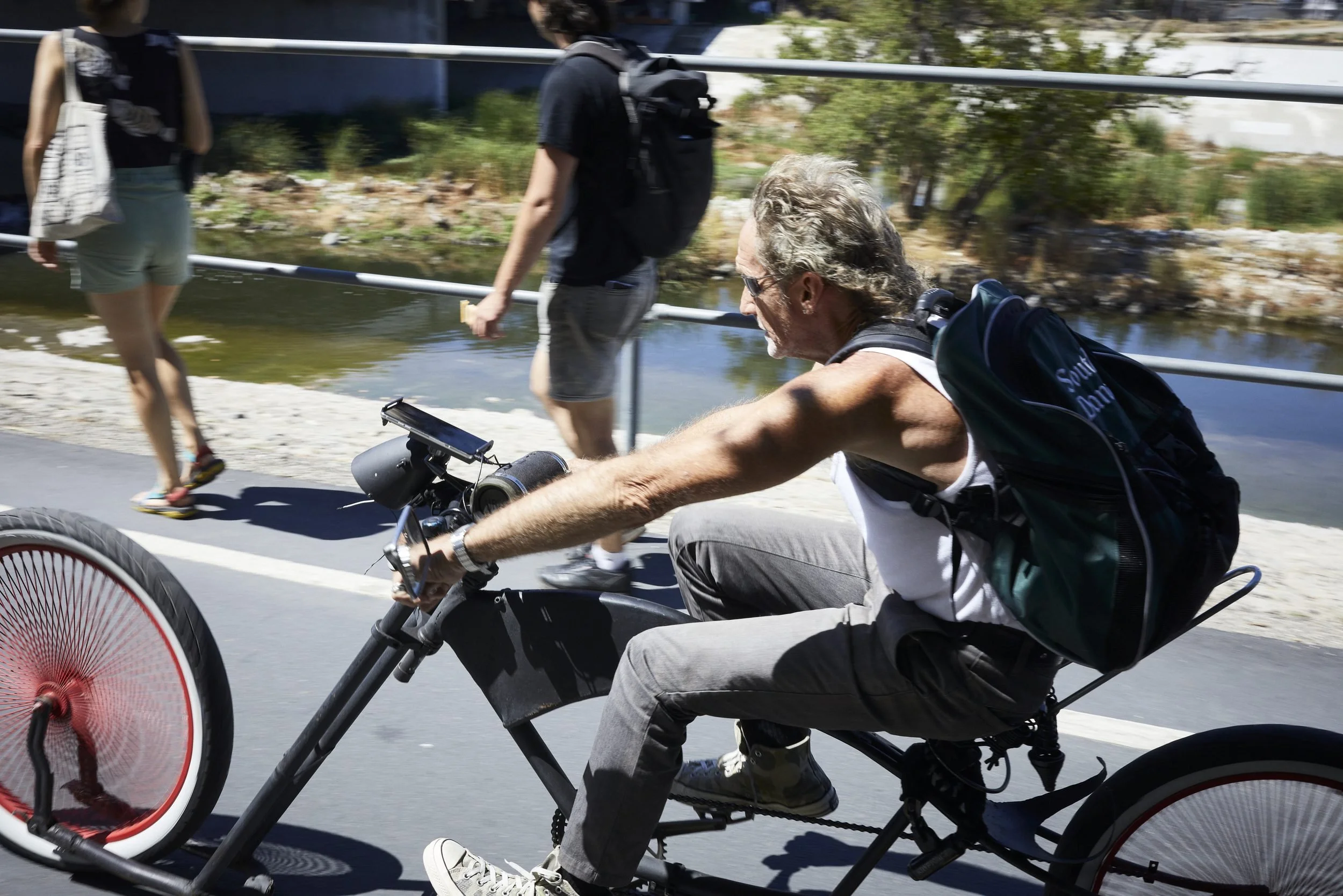 Man riding a recumbent trike on a paved path near water, with spectators in background.