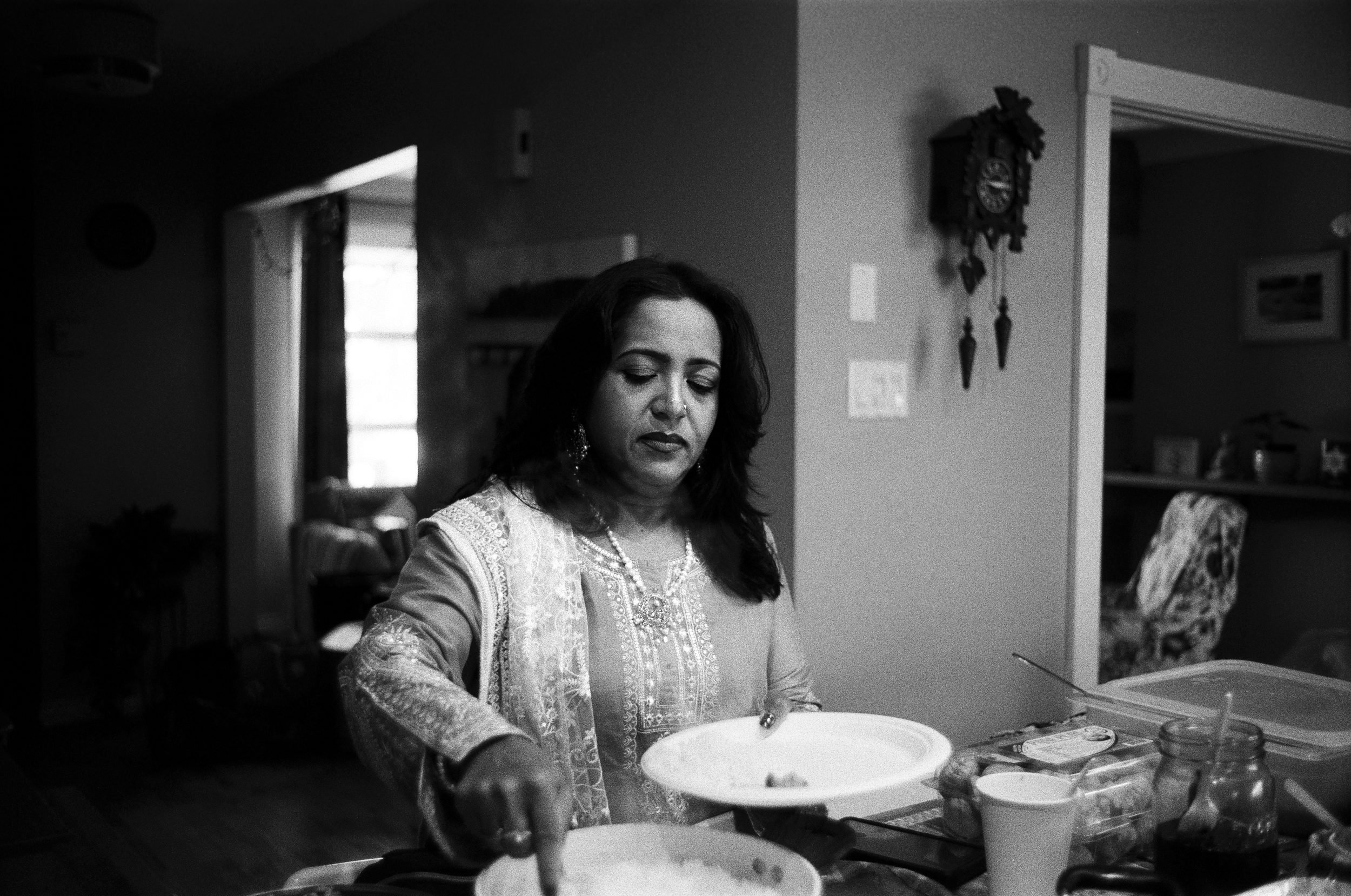Woman in embroidered clothing preparing food at a kitchen counter in black and white.