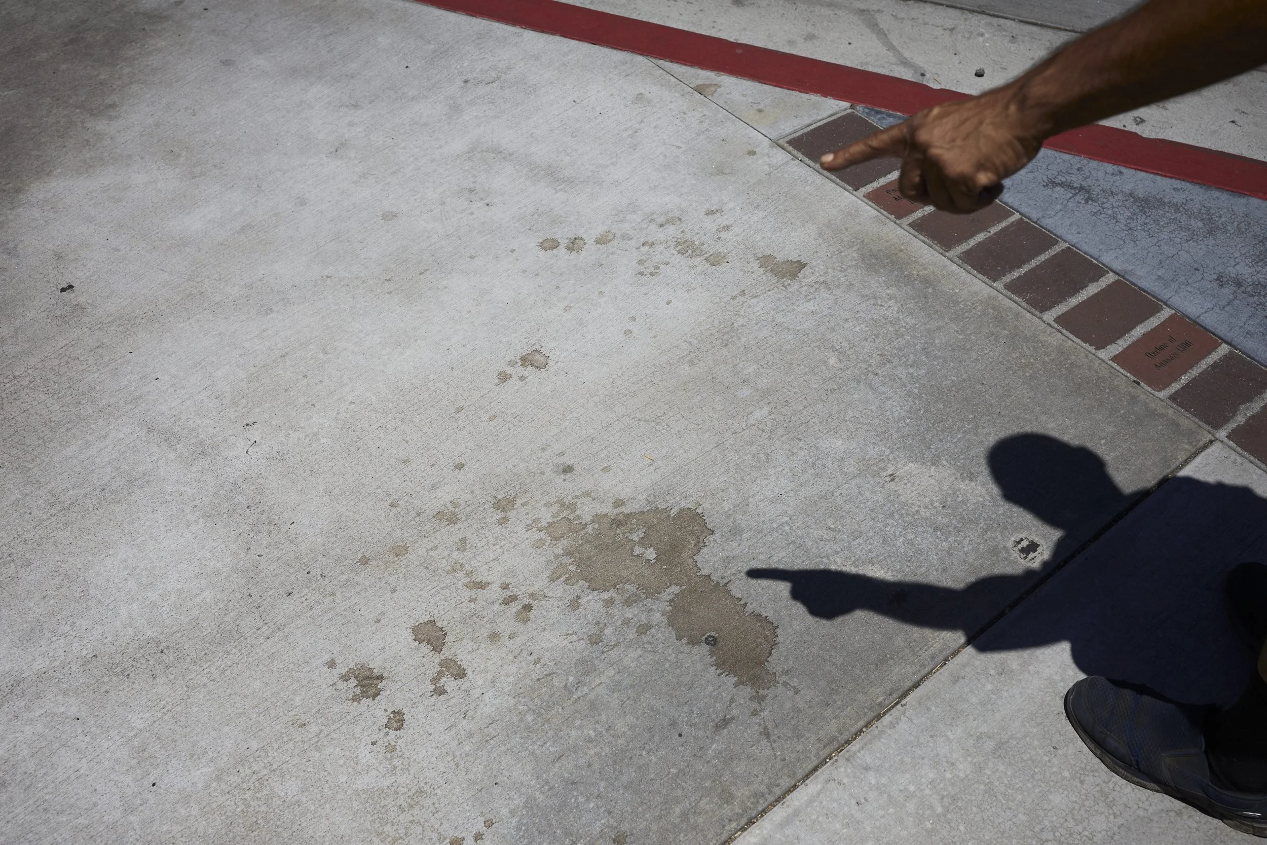 A person points to wet stains on a concrete floor next to a red and white striped border.