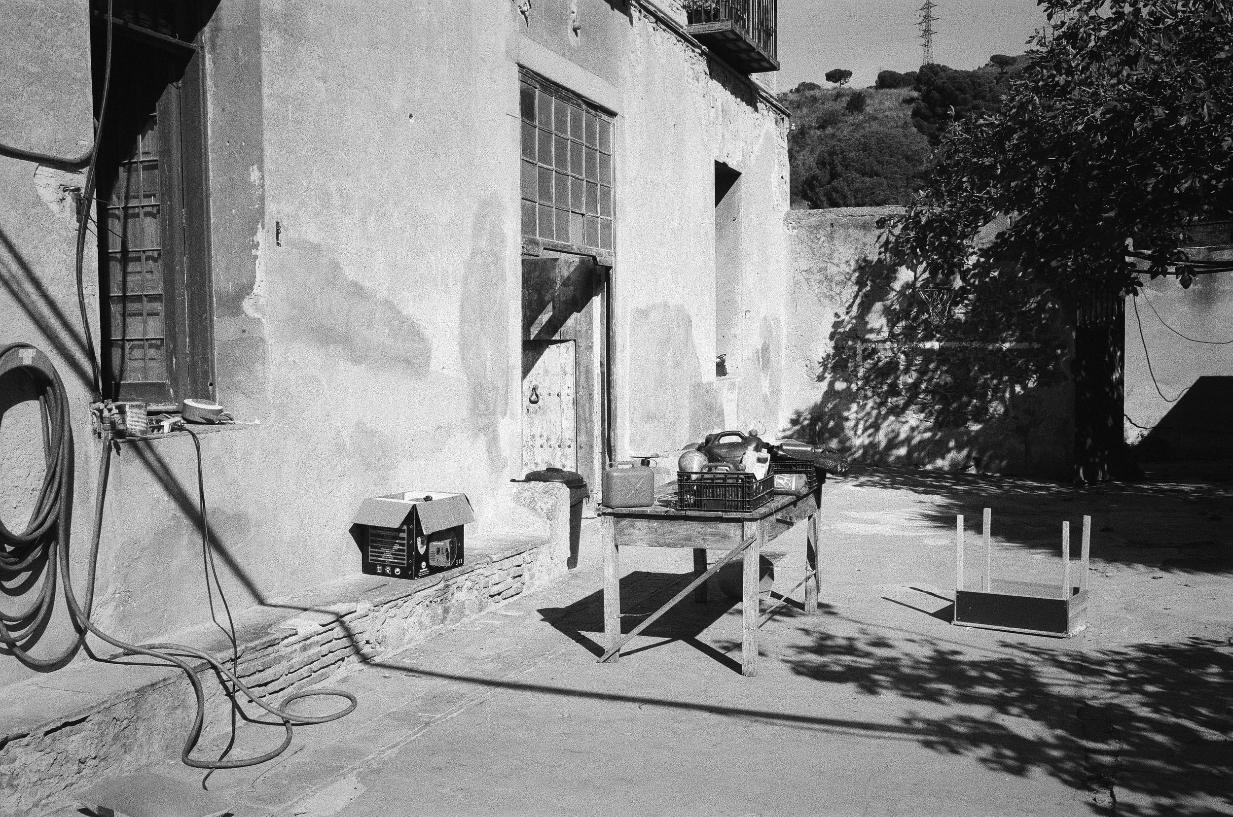 A white-walled building with a typewriter on a table outside, surrounded by coiled cables and vegetation.