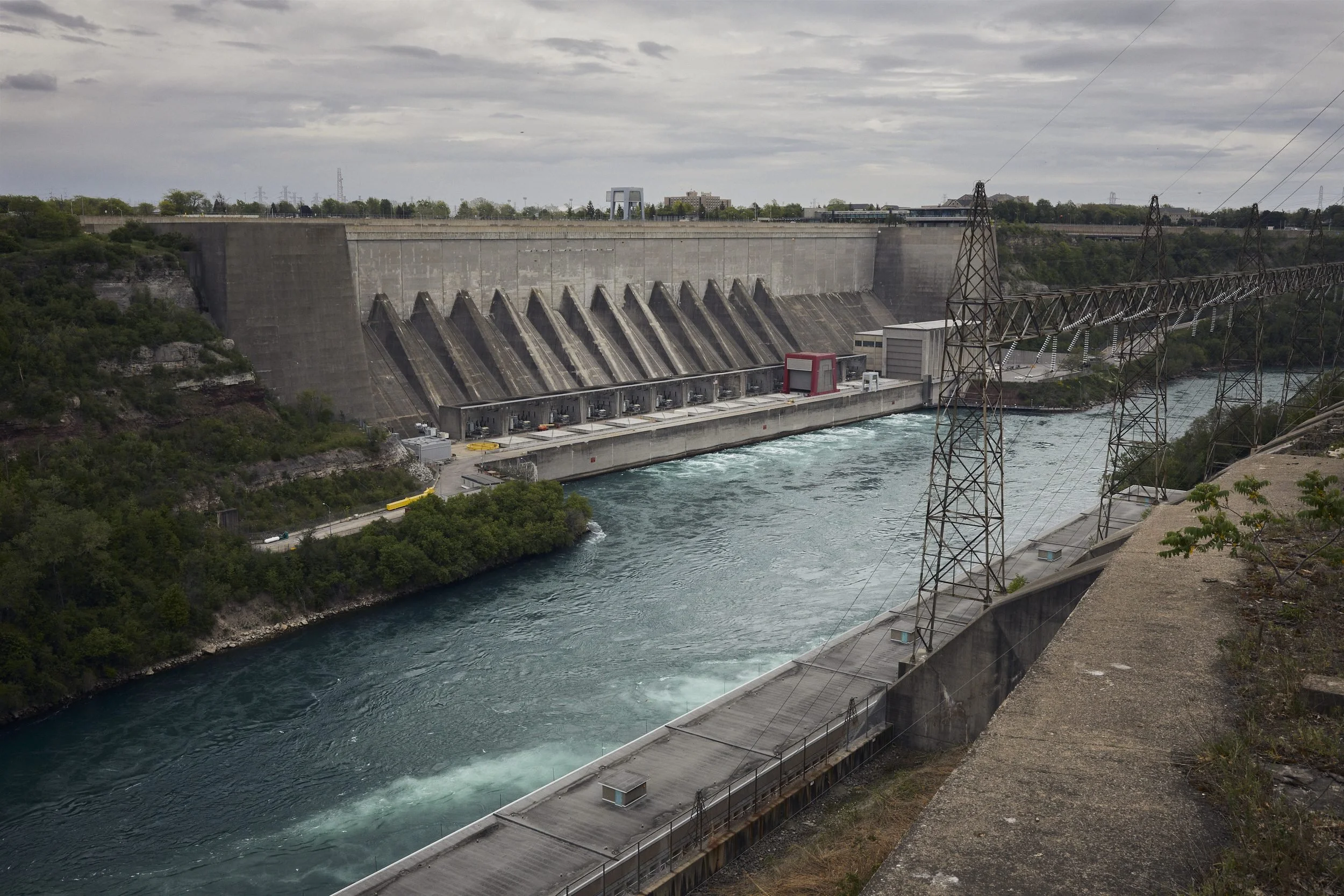 Hydroelectric dam with spillway gates spanning a turquoise river, flanked by electrical transmission towers.