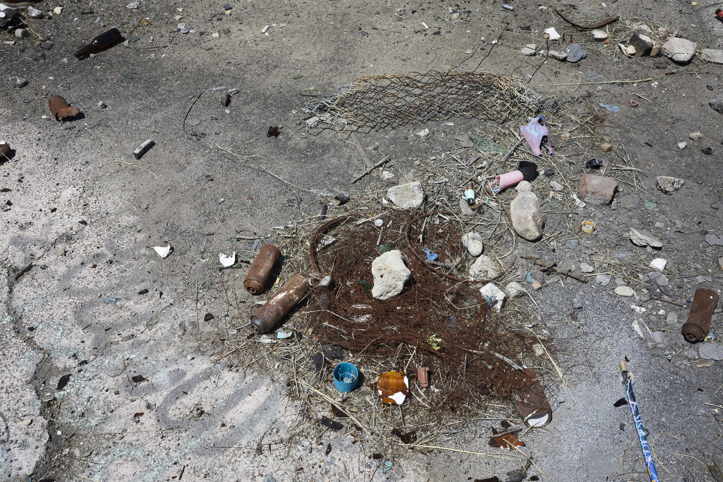 Discarded bottles, shells, and debris scattered on pavement and sand.
