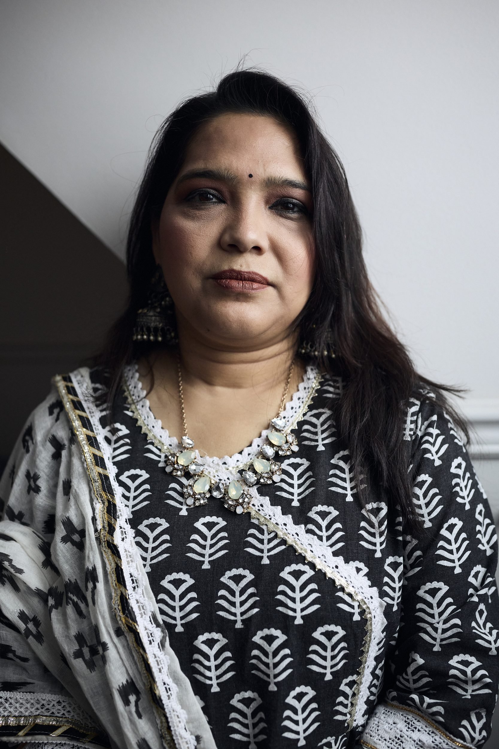 Woman wearing a black and white patterned kurta with white lace trim and jewelry, photographed against a plain wall.