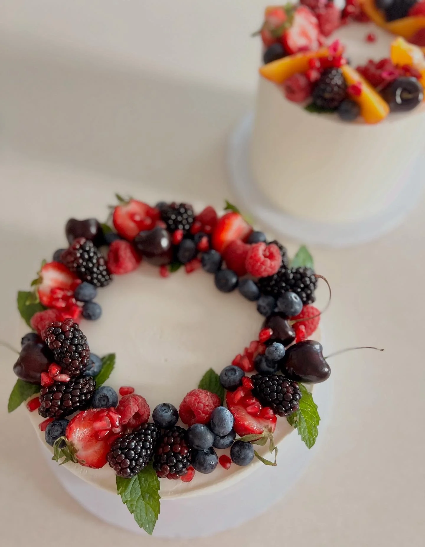 A cake decorated with mixed berries, including strawberries, blackberries, blueberries, and garnished with green mint leaves.