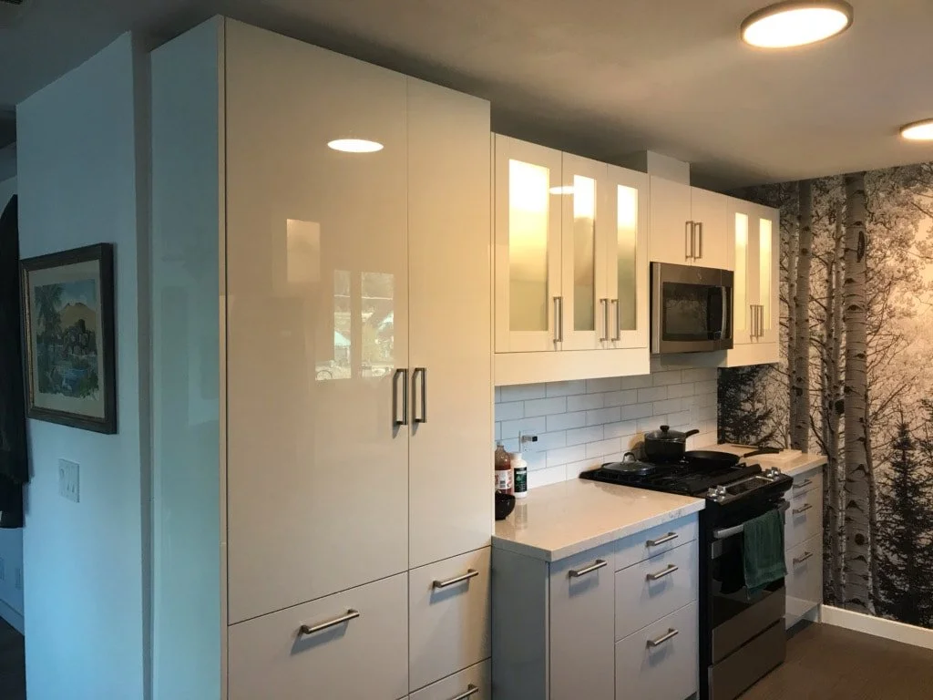 Modern kitchen with white cabinets, stainless steel handles, a built-in microwave, stove with a pot, and a backsplash with white subway tiles. A wall features a large forest mural with trees.