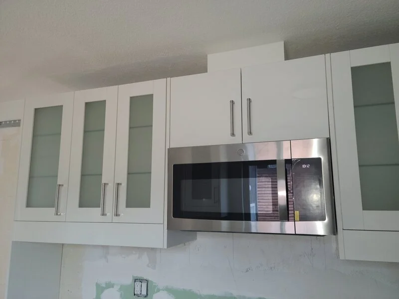 White kitchen cabinets with glass doors above and a built-in stainless steel microwave oven