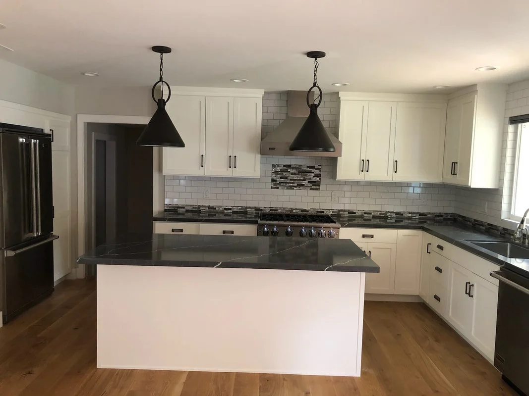 Modern kitchen with white cabinets, black countertops, stainless steel appliances, and pendant lights.