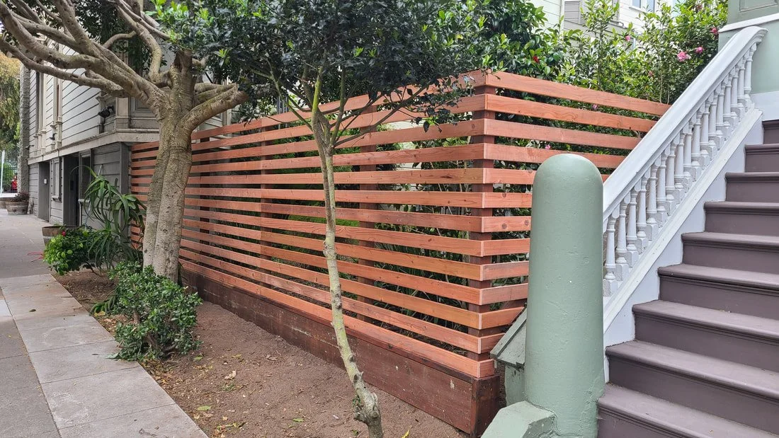 Wooden slat fence near stairs and trees in a residential yard.