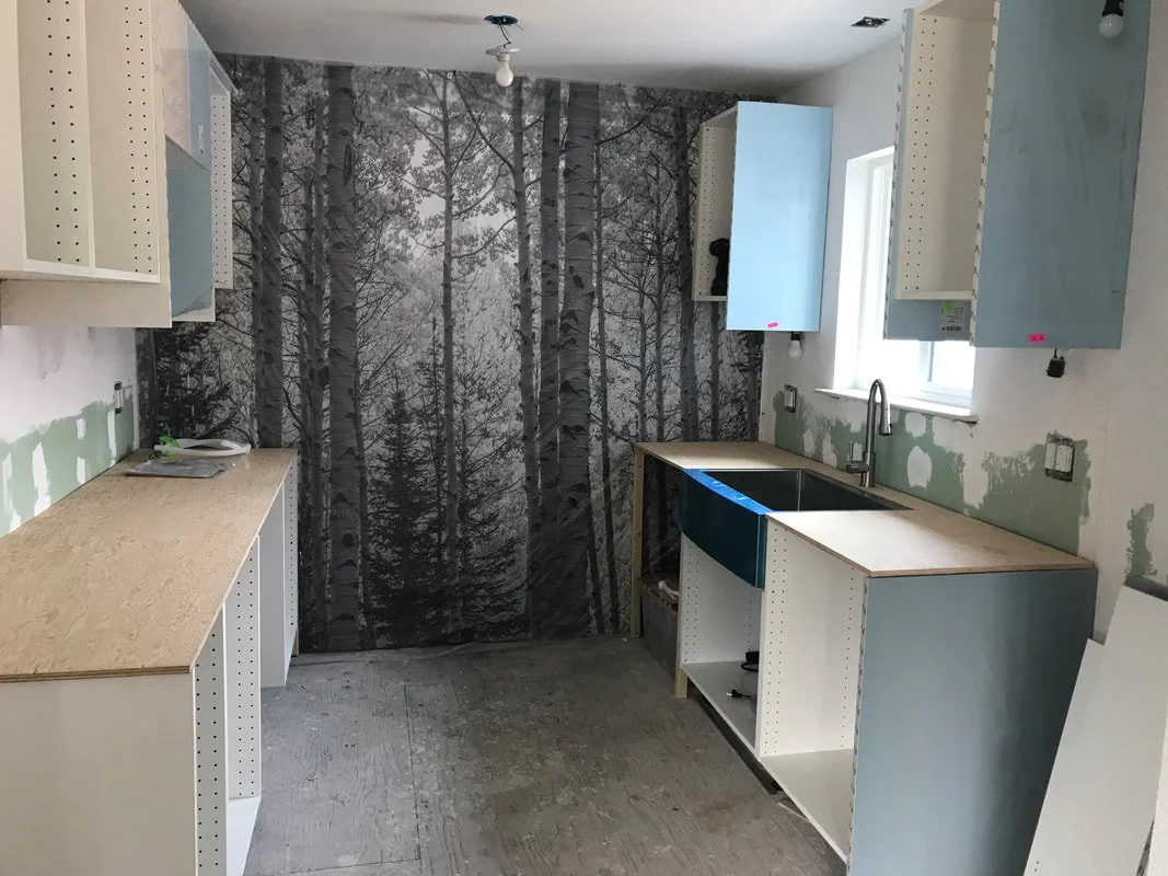 A kitchen under construction with partially installed cabinets and a forest-themed wallpaper on the back wall.