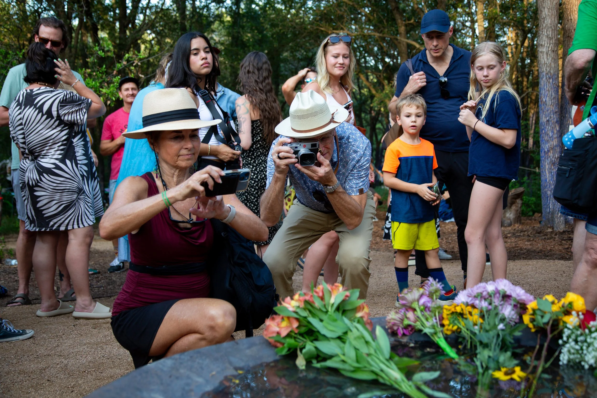 People take pictures of flowers placed into Malin's stone bowl fountain to honor the wooden troll during a memorial service at Pease Park on June 24, 2026. 