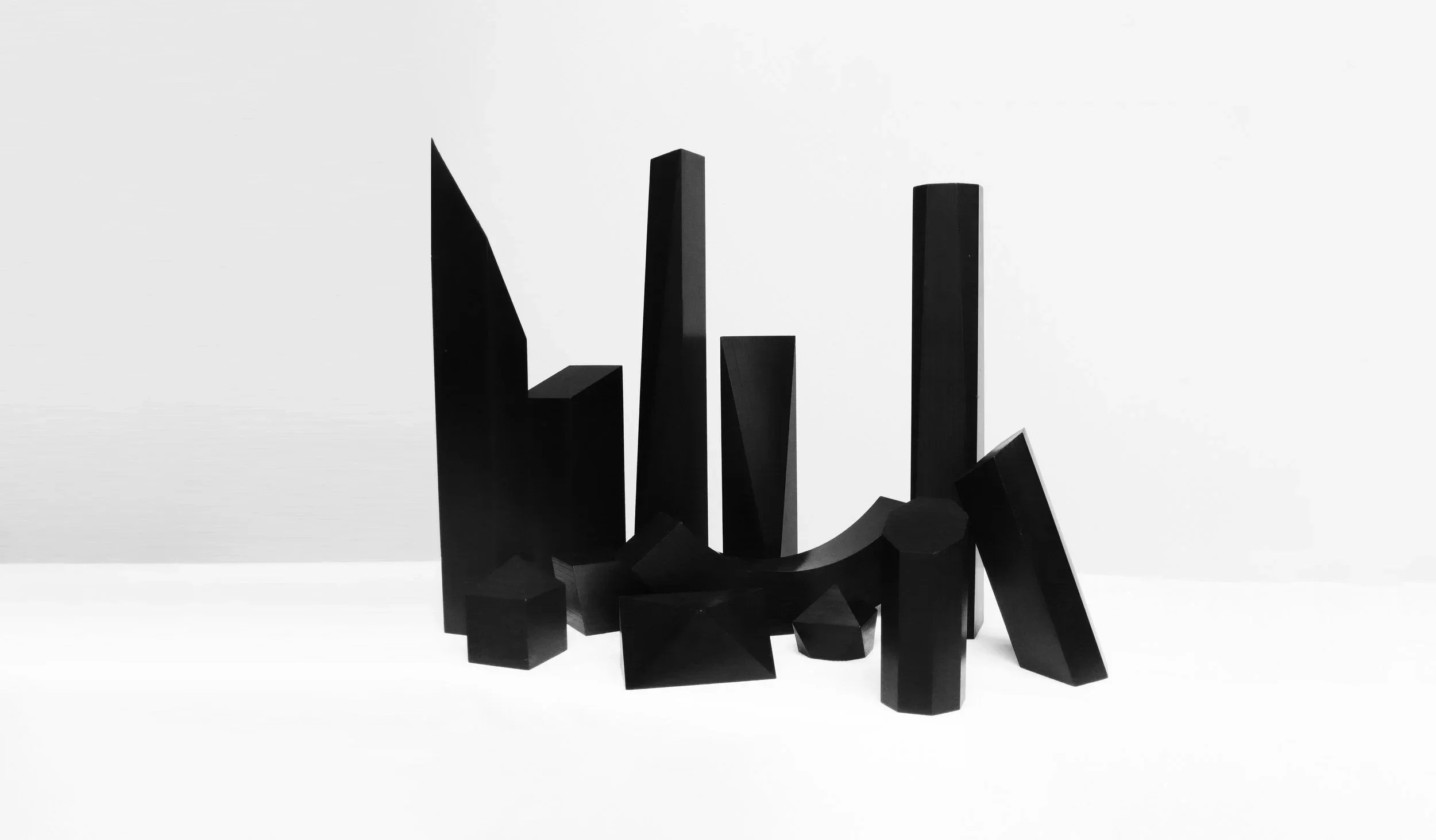 An arrangement of matte black geometric sculptures, showcased in a minimalist gallery setting against a plain white background.