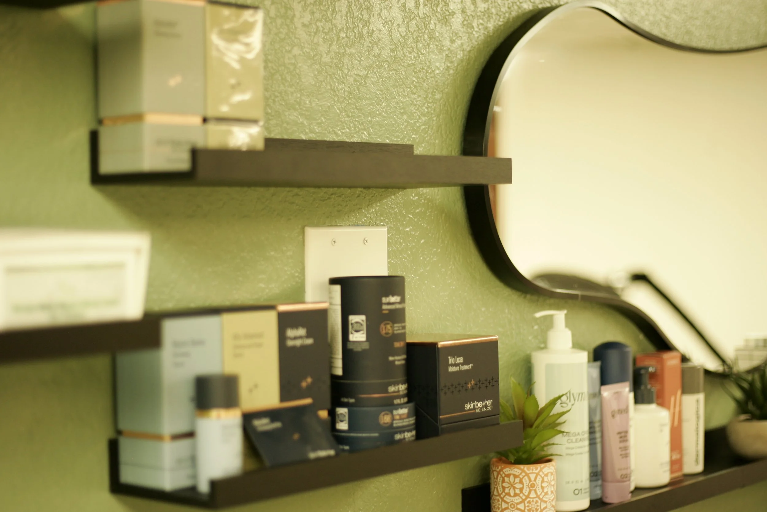 A bathroom shelf with various skincare and beauty products arranged on it, including creams, bottles, and containers, with a small potted plant below the shelf.