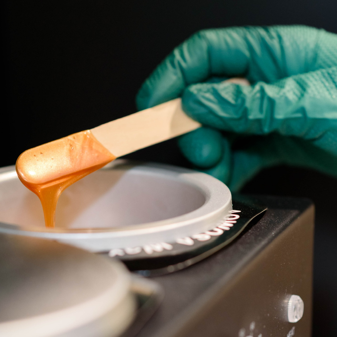 Close-up of a hand wearing a green glove using a wooden spatula to pour caramel into an ice cream maker.