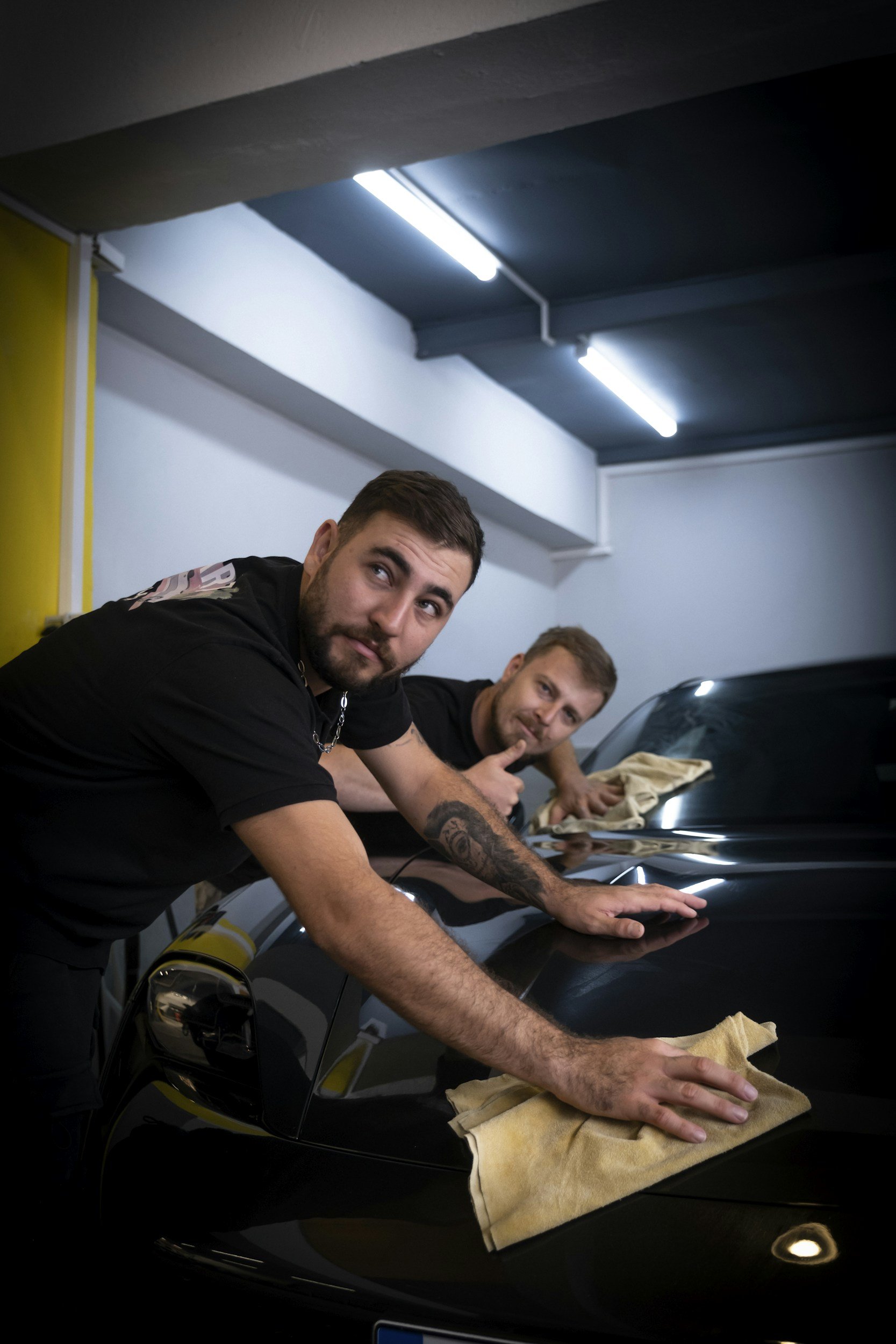 two detailers wiping down car hood