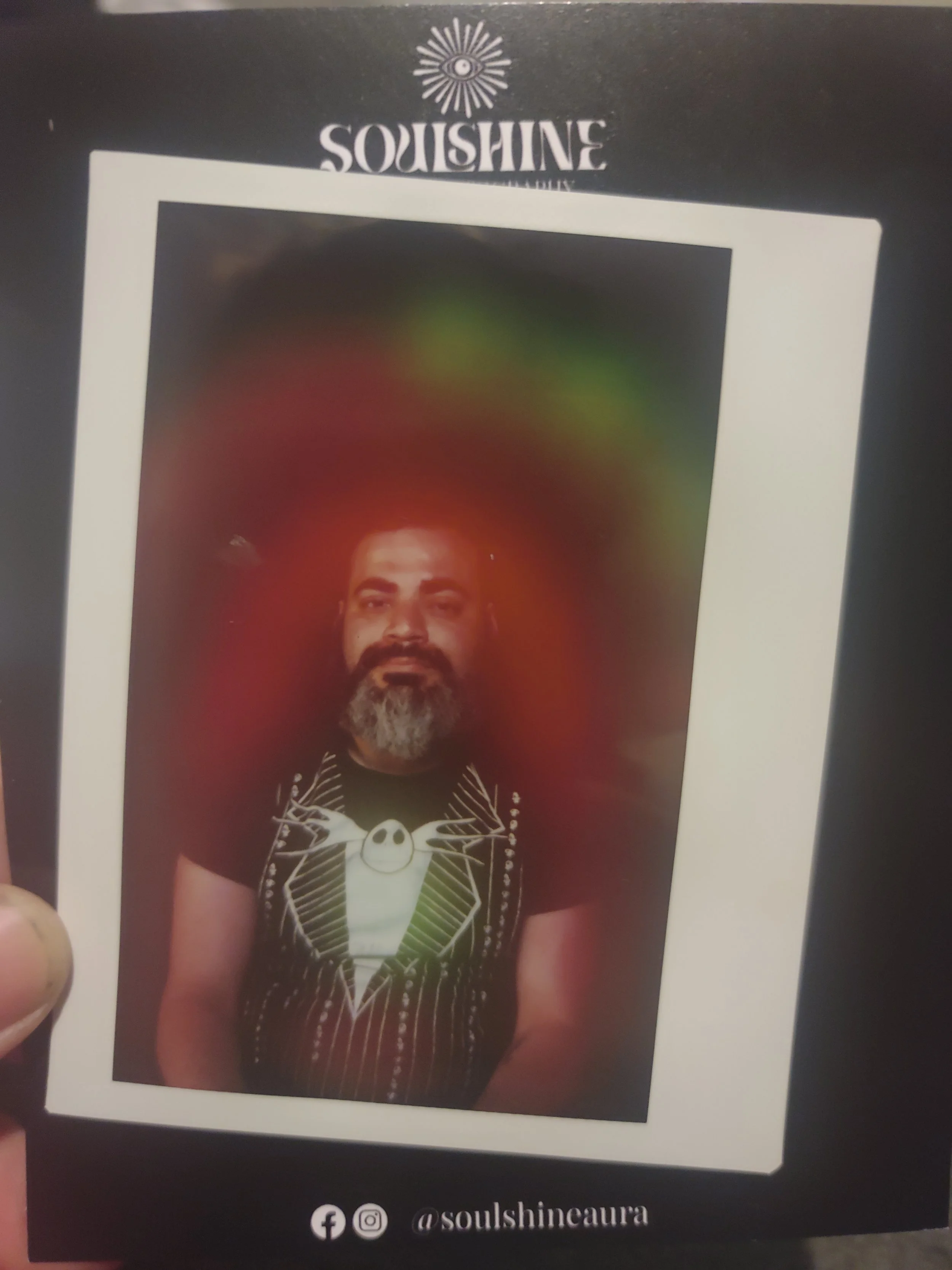 A person with a beard and mustache, wearing a black t-shirt featuring Jack Skellington from 'The Nightmare Before Christmas,' is shown on a glossy card with a black background. The card displays the brand name 'SQUISHINE' at the top, a logo of an eye with rays, and the social media handle '@soulshinceaura' at the bottom.
