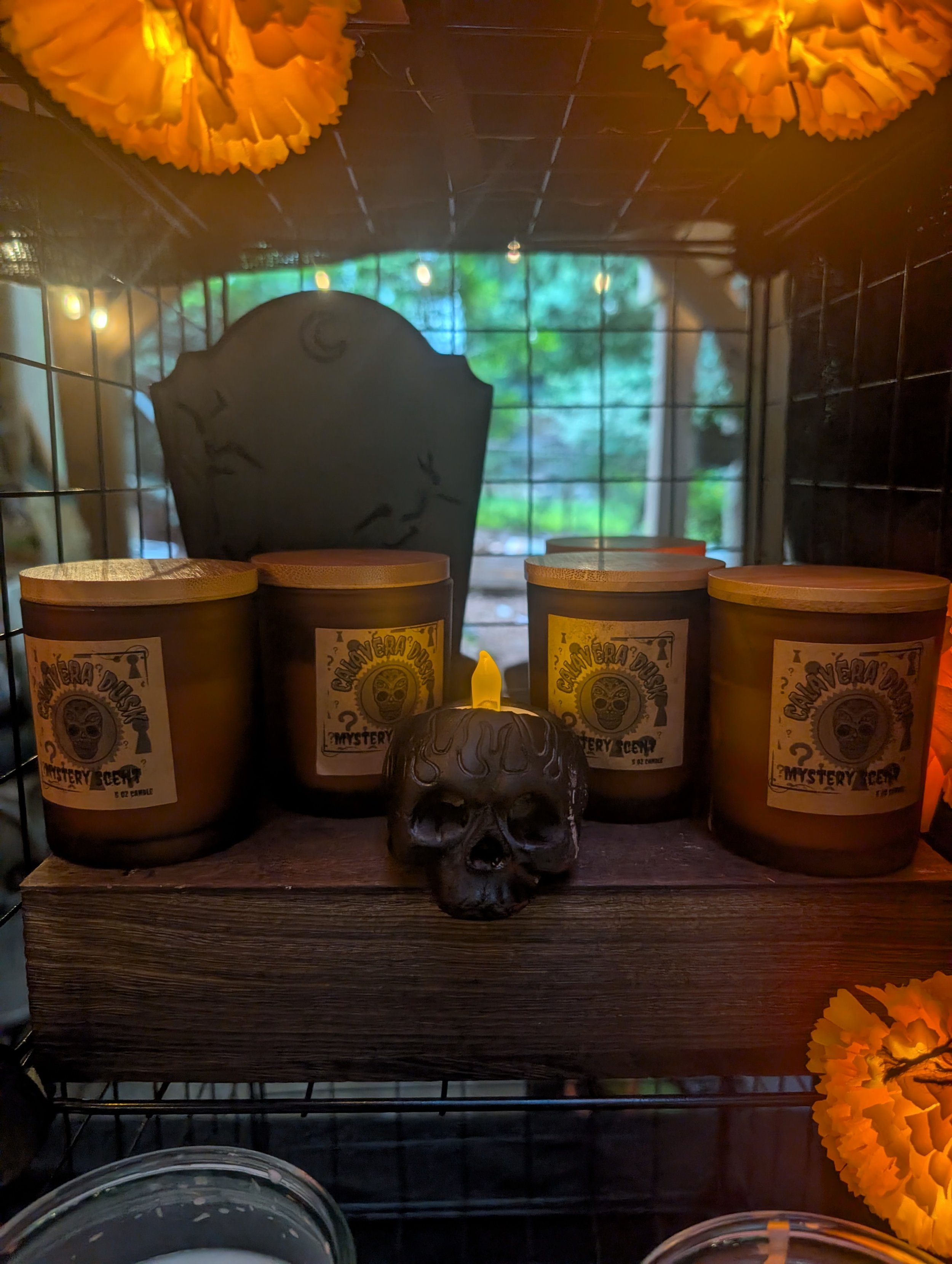 Shelf with Halloween-themed items including candles labeled 'Mystery', decorative skull, and orange flowers, with a window in the background