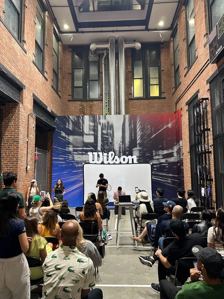 An indoor Wilson event with a presentation area, seated audience, and a large industrial-style ceiling with metal pipes.