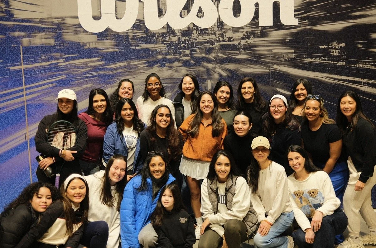 A group of women and girls posing for a photo in front of a large background with the word 'Clarison' at a tennis event, some holding tennis rackets, smiling, and dressed casually.