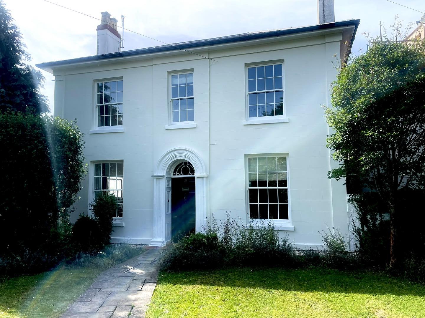 A white, three-story house with large windows and a decorative arched front door, and five sash windows.