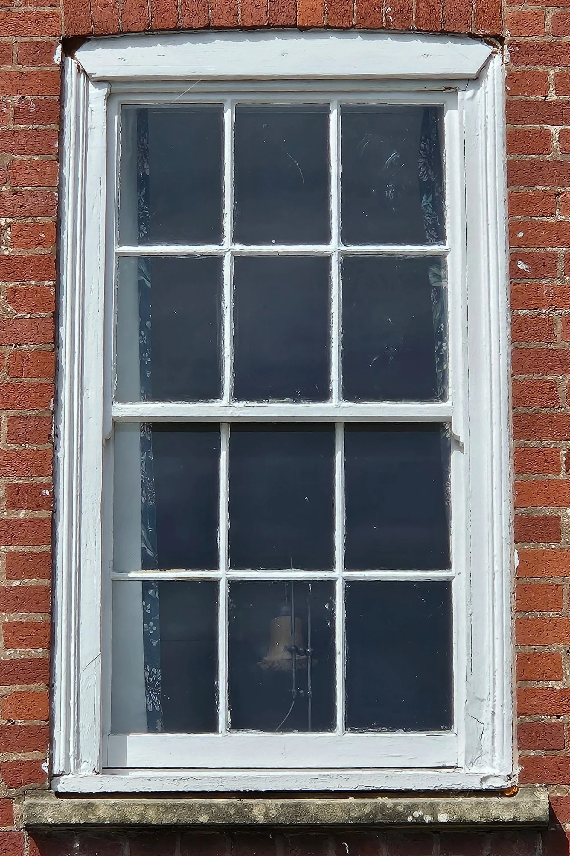 A white wooden window with multiple small panes set in a brick wall. The window appears aged and slightly weathered.