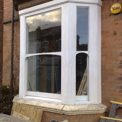 A new bay window installed on a brick house with a white frame, reflecting the cloudy sky and surrounding buildings.