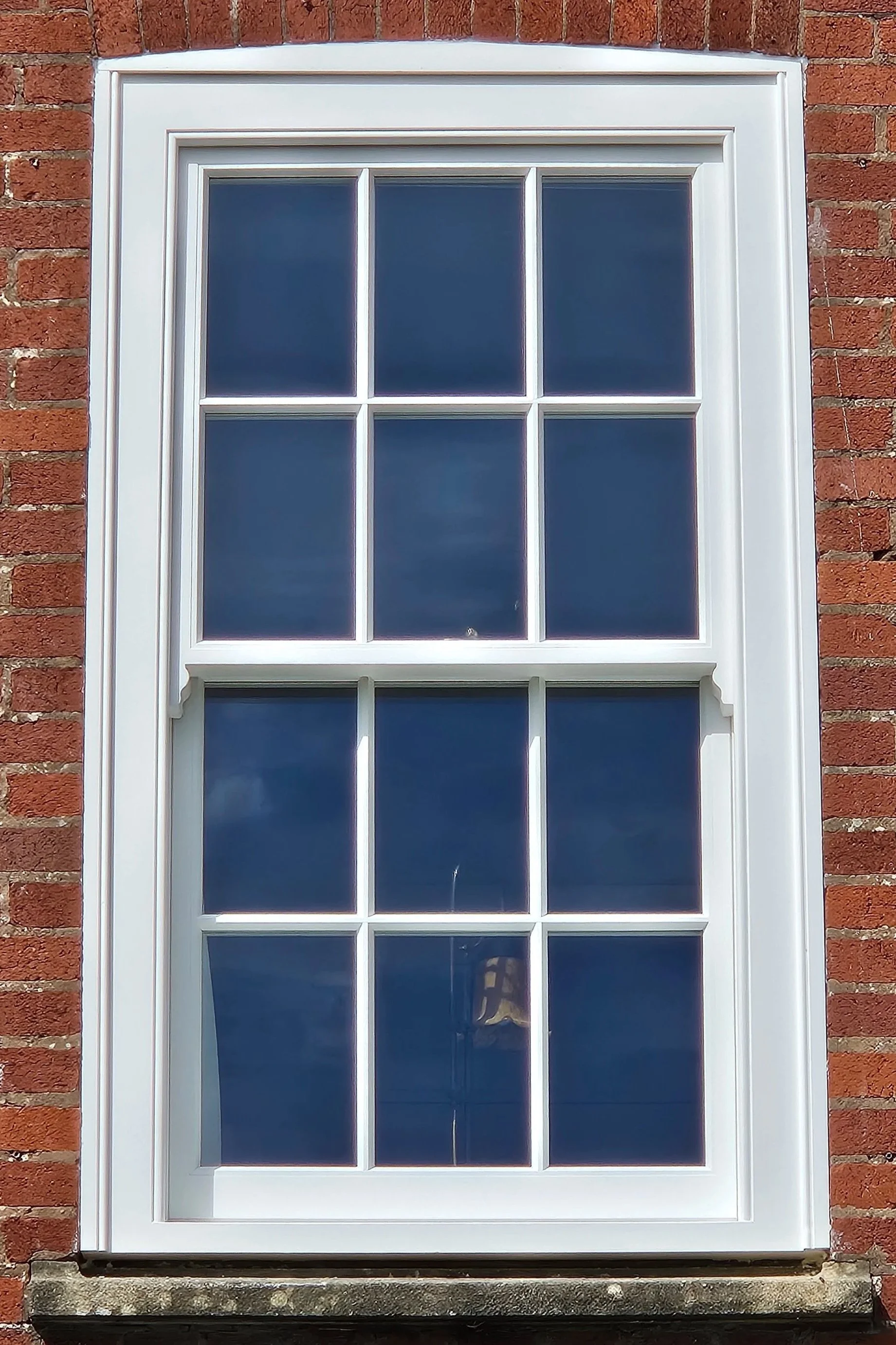 A white-framed window with six panes set in a red brick wall.
