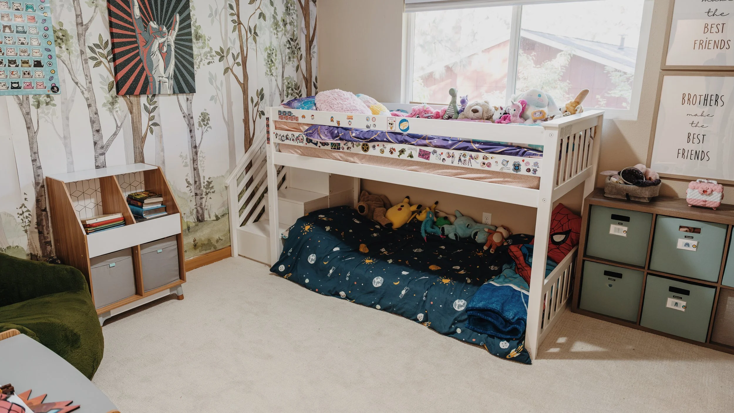 A child's bedroom with a white loft bed filled with stuffed animals, a drawing of a dog on the wall, a bookshelf, and storage bins, with large windows allowing sunlight.