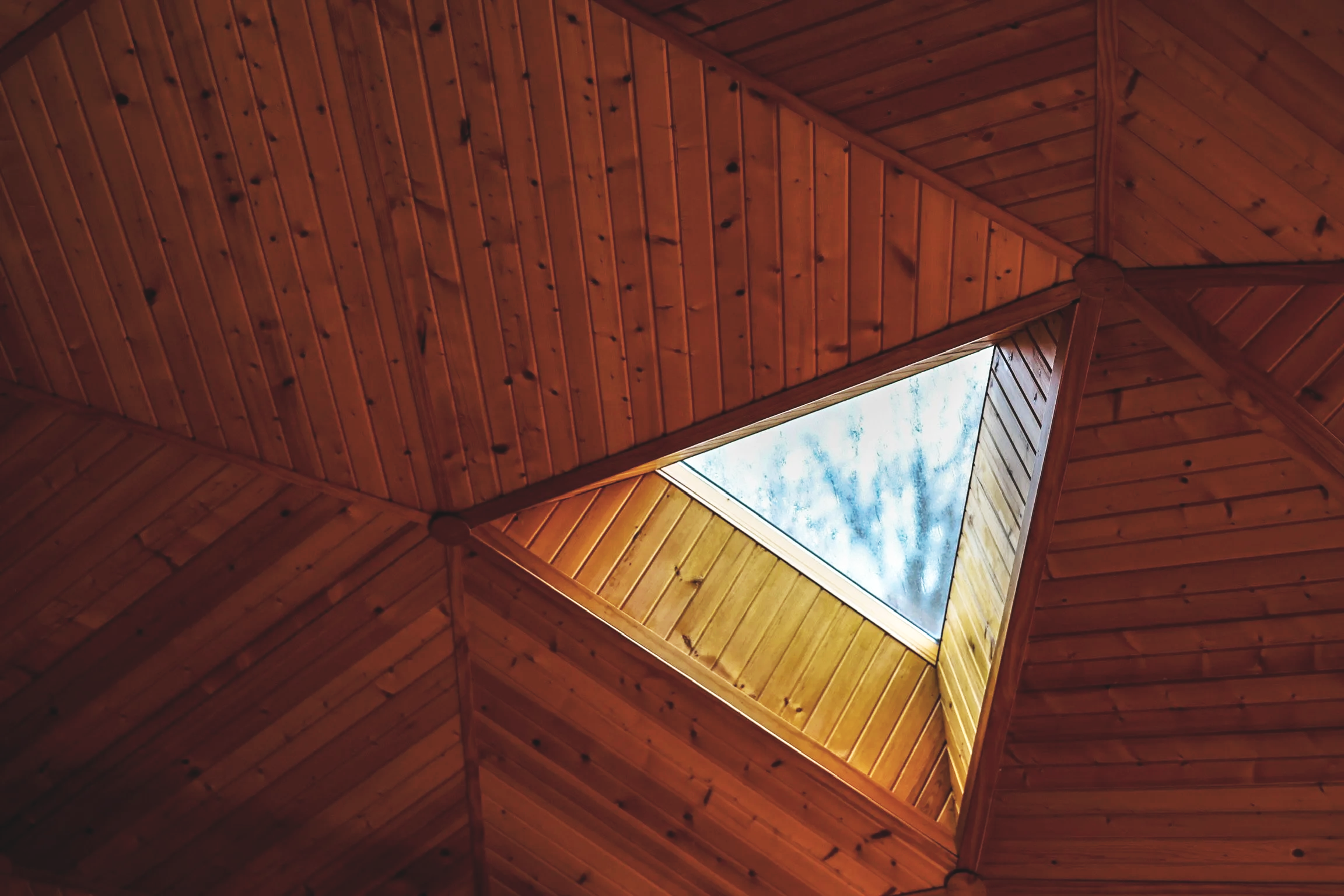 A wooden ceiling with a square opening revealing the sky and clouds above.