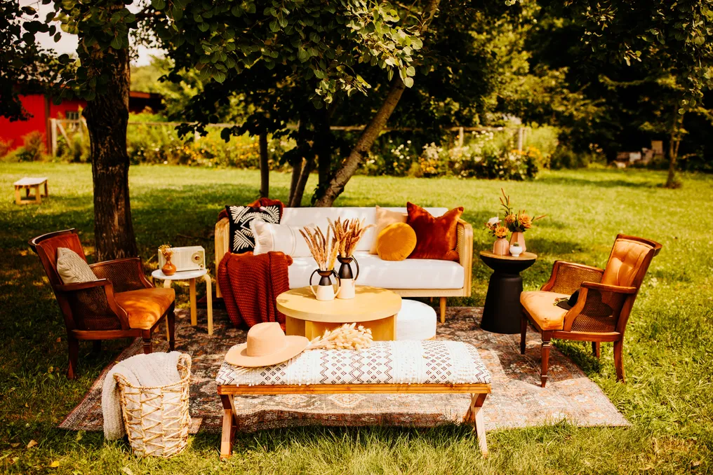 Outdoor patio seating area with vintage chairs, a white couch, a rug, and decorative pillows surrounded by trees and greenery.
