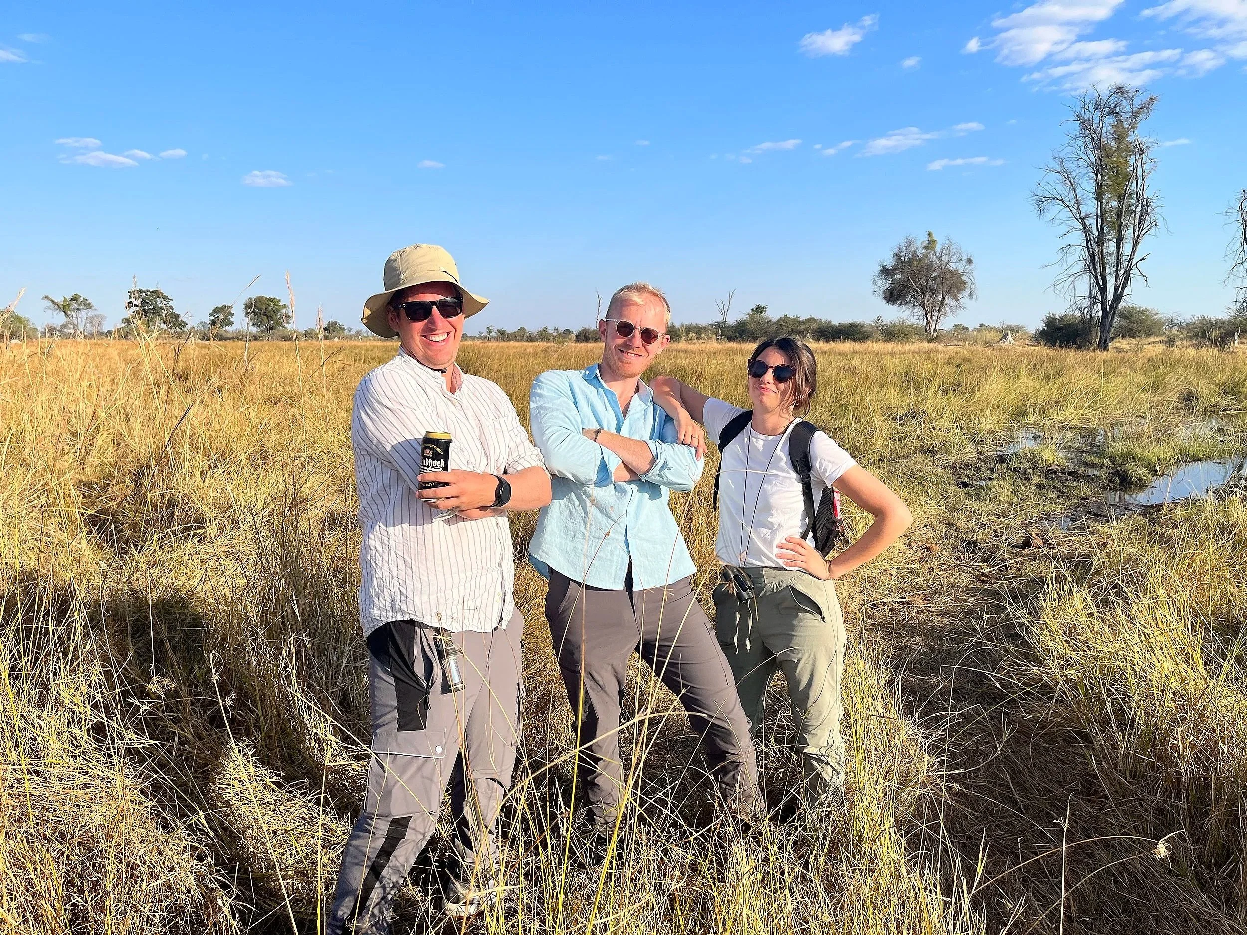 Three smiling guests standing together in a grassy field in the Okavango Delta, Botswana