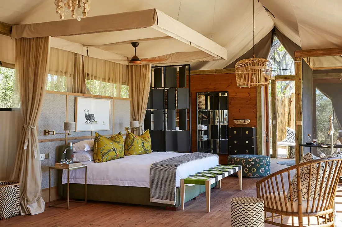 A spacious, luxurious tented bedroom suite featuring a king-sized bed with white linens, pattern pillows, a wooden floor, and a seating area.
