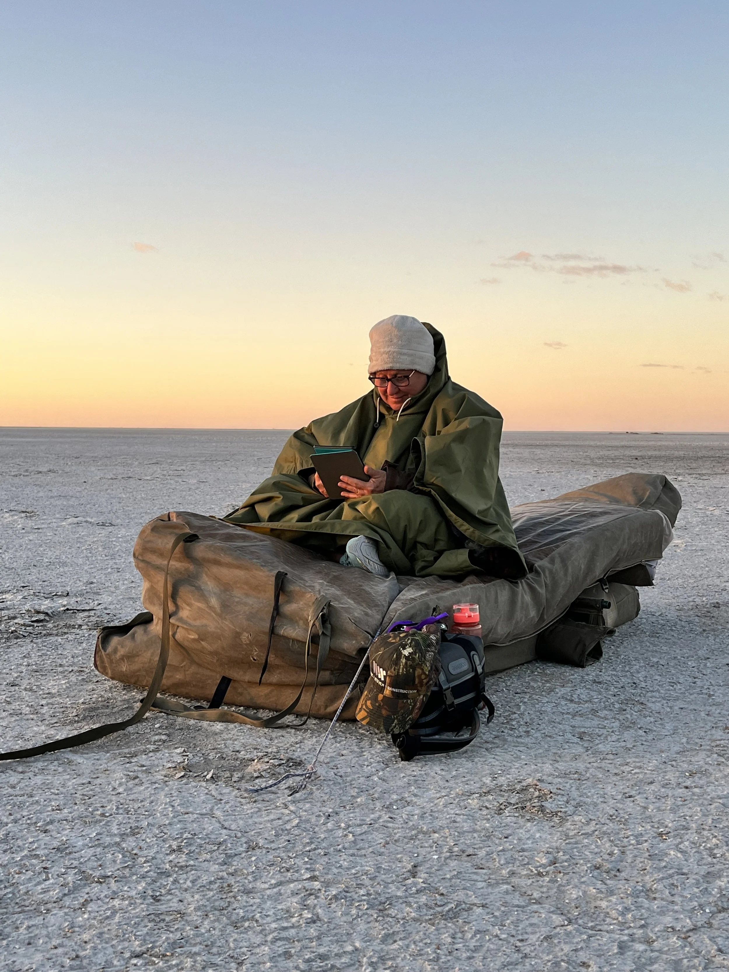 A guest reading a book in her bedroll as the sun rises over the Makgadikgadi Salt Pans, Botswana.