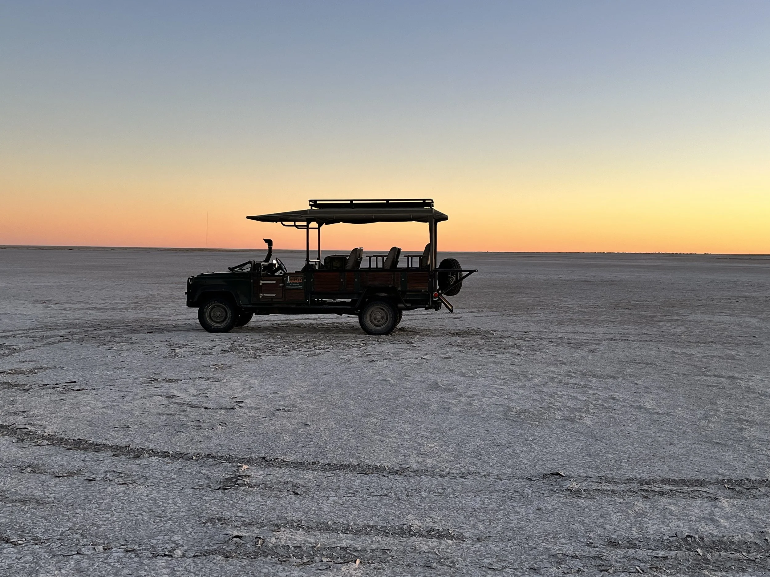 A game drive vehicle on the Makgadikgadi Salt Pans as the sun sets creating a blend of red to blue across the sky.