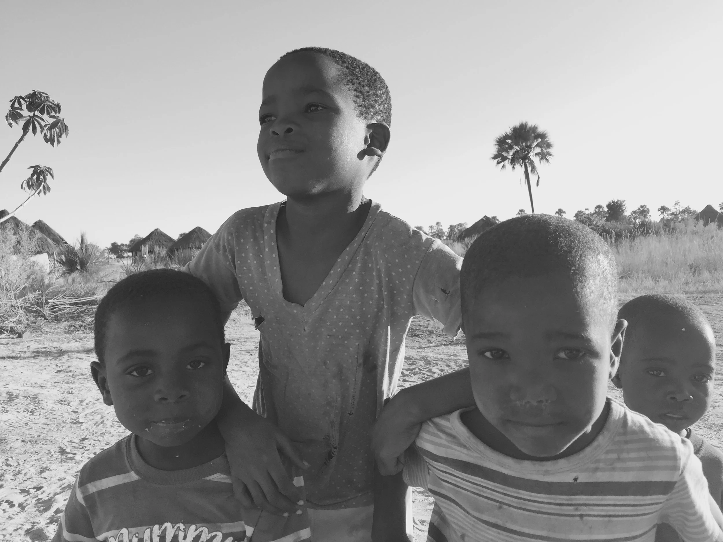 Four children in front of traditional huts at the Boro Village on the edge of the Okavango Delta, Botswana