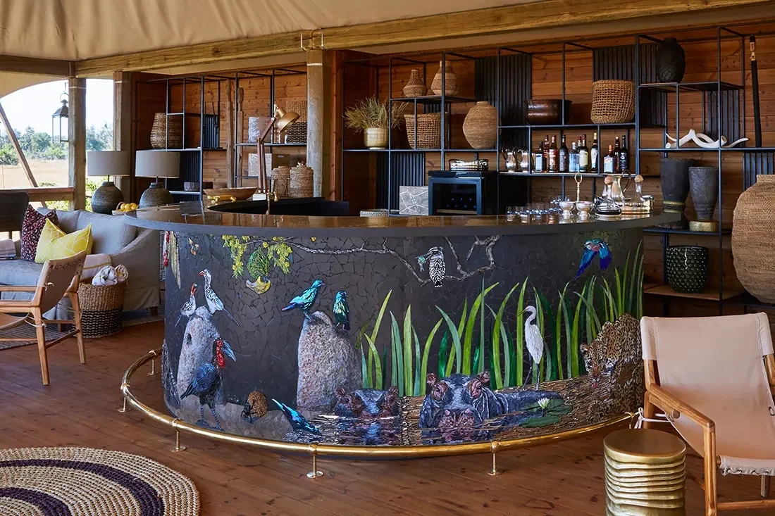 A curved safari bar featuring a colorful mural of African birds and wildlife, stocked with bottles and glassware behind the counter.