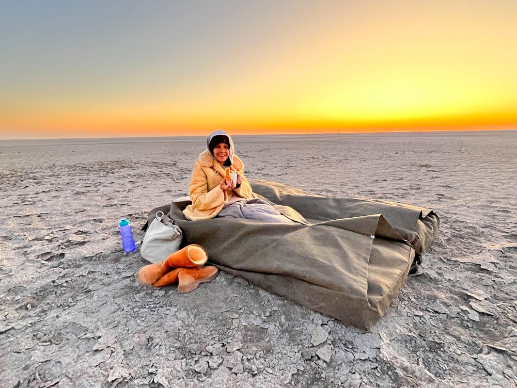 A guest drinking an early morning coffee with a rusk in her bedroll on the Makgadikgadi Salt Pans, Botswana.