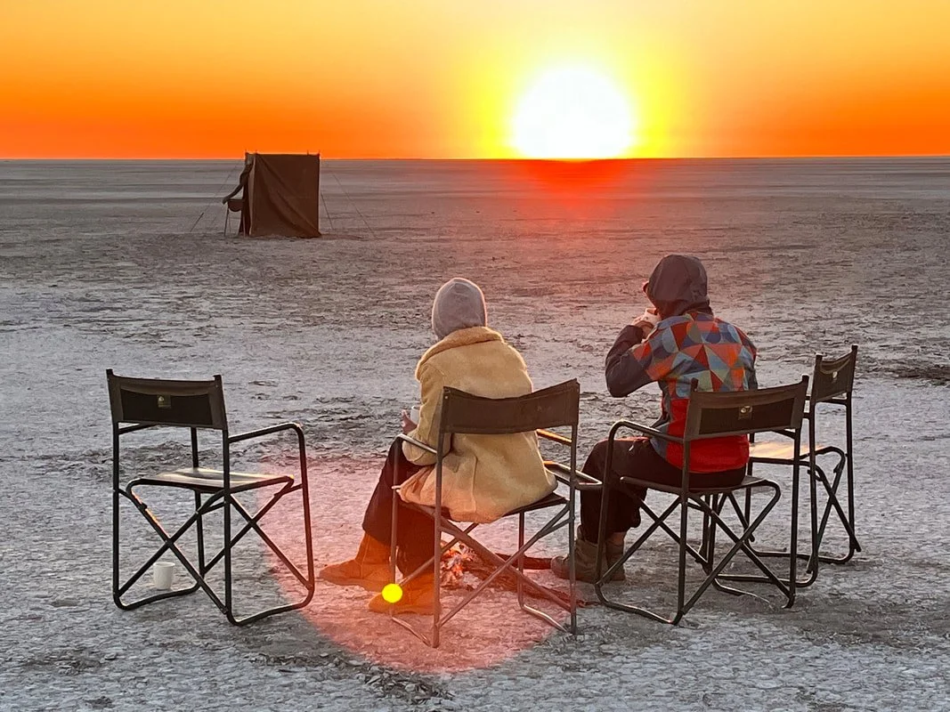 Two guests sitting and watching the sun set on the Makgadikgadi Salt Pans, Botswana.