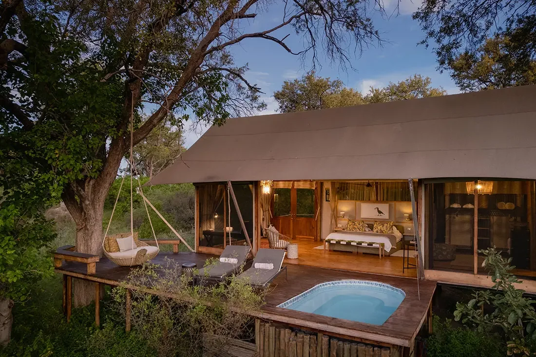 Exterior view of a luxury tented bedroom at dusk, featuring a private wooden deck with lounge chairs and a small plunge pool.