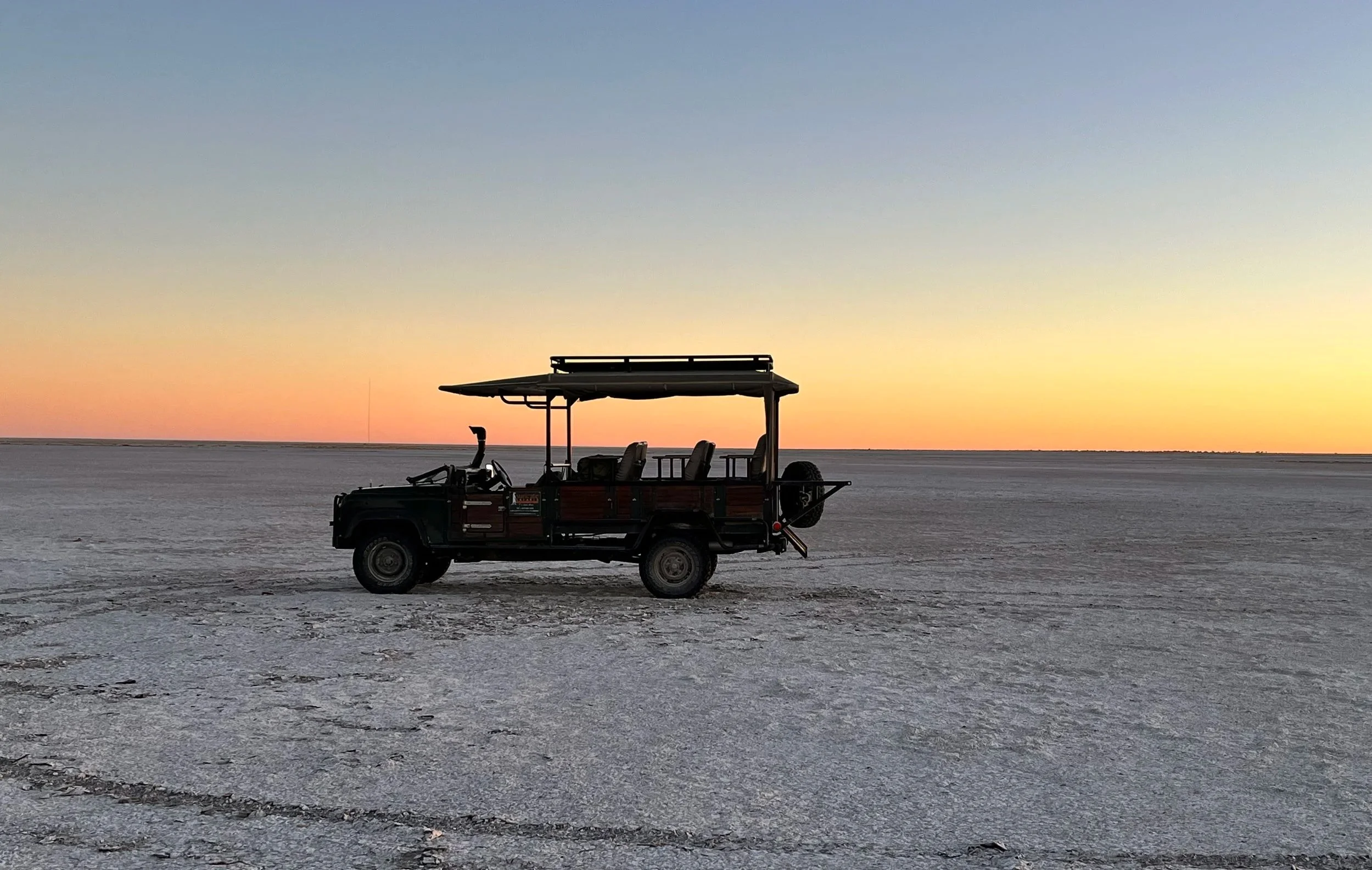 A game drive vehicle on the Makgadikgadi Salt Pans as the sun sets creating a blend of red to blue across the sky
