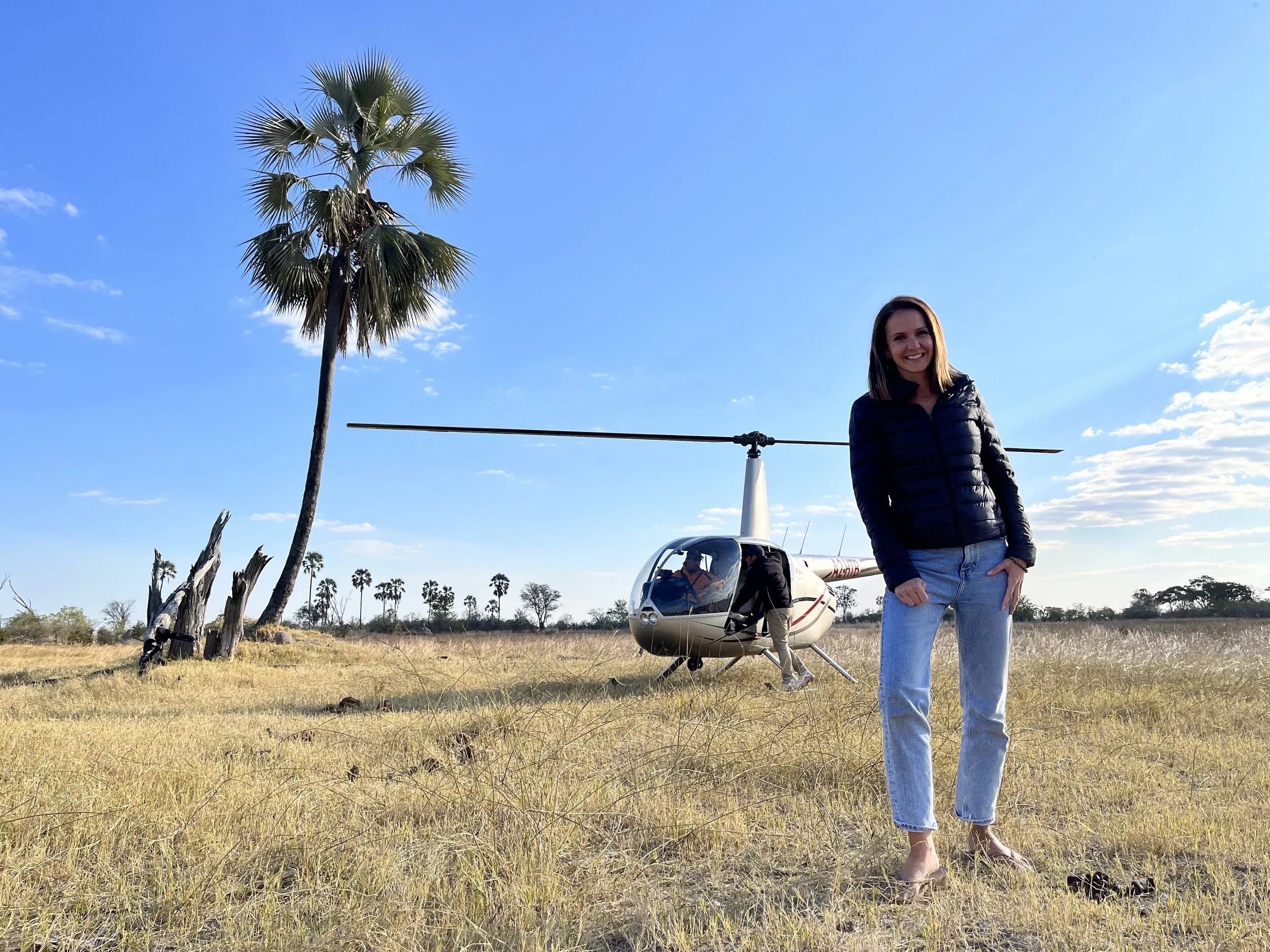 A smiling guest standing in front of a helicopter in a grassy clearing in the Okavango Delta
