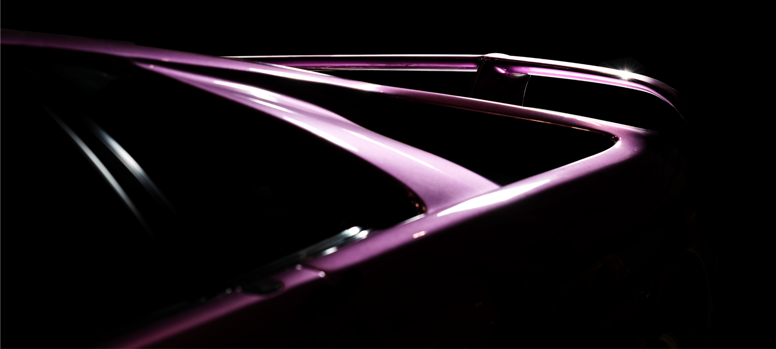Close-up of a purple sports car with sleek design, glossy surface, and reflecting light, shown in a dark setting.