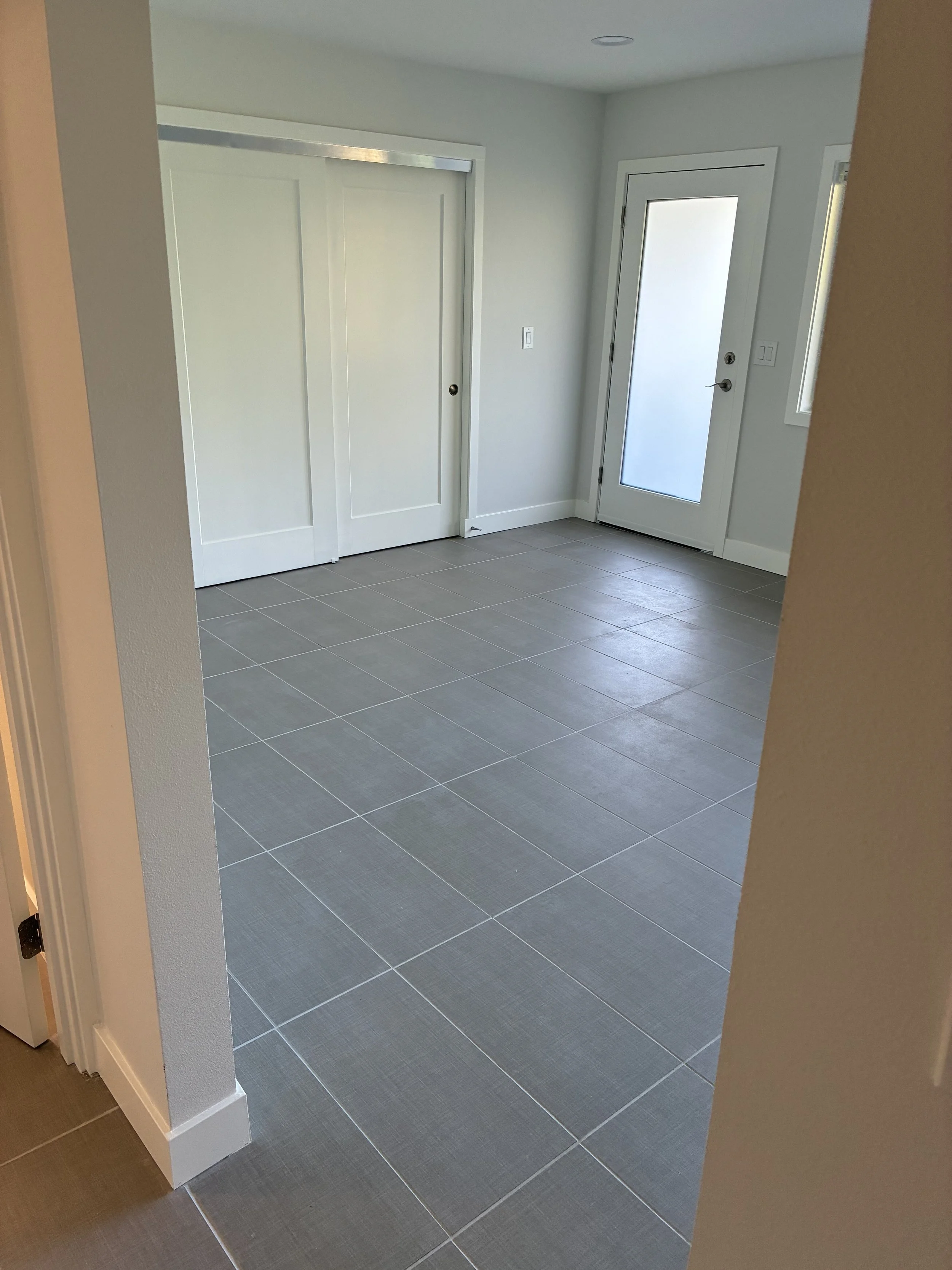 A room with a door that has frosted glass, adjacent to a closet with sliding doors, and light gray tiled flooring.